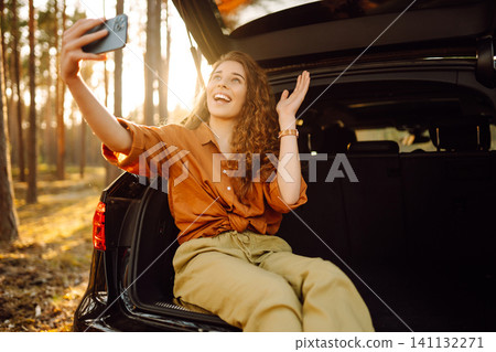 Woman is resting in trunk of car with phone. Concept of traveling by car, active lifestyle. Woman is resting in trunk of car with phone. Concept of traveling by car, active lifestyle. 141132271