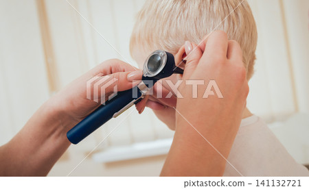 Doctor examines ear with otoscope in a pediatrician room. 141132721