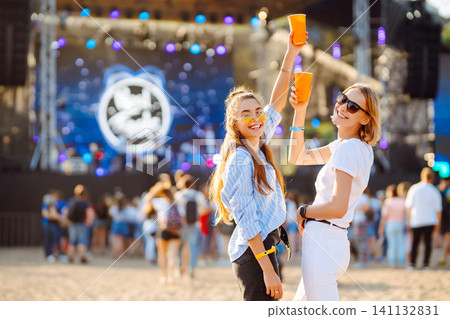Two woman having great time at music festival. Girlfriends rinking beer at Beach party. Lifestyle. 141132831
