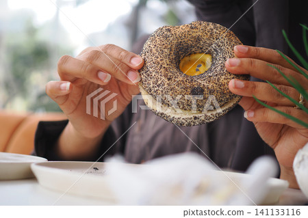 Enjoying a delicious bagel with poppy seeds in a cozy cafe 141133116