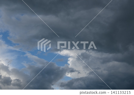 Dense layer of dark storm clouds indicating approaching storm activity with visible blue sky gaps Dense layer of dark storm clouds indicating approaching storm activity with visible blue sky gaps 141133215