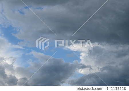 Overcast sky with dense gray clouds and small gaps of blue sky visible between the dark clouds 141133218