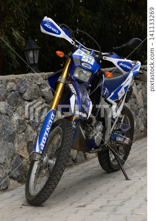 Gaziveren Cyprus -02.04.2025 Stylish blue dirt bike parked beside a stone wall in an outdoor setting during daylight hours Gaziveren Cyprus -02.04.2025 Stylish blue dirt bike parked beside a stone wall in an outdoor setting during daylight hours 141133269