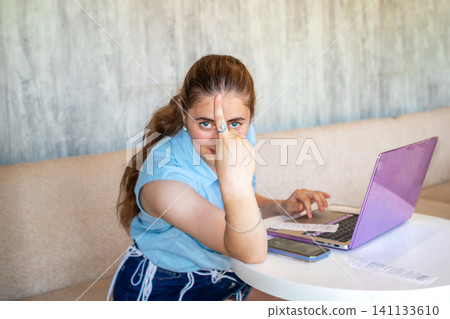 Young woman giving middle finger to camera while working on laptop at home Young woman giving middle finger to camera while working on laptop at home 141133610