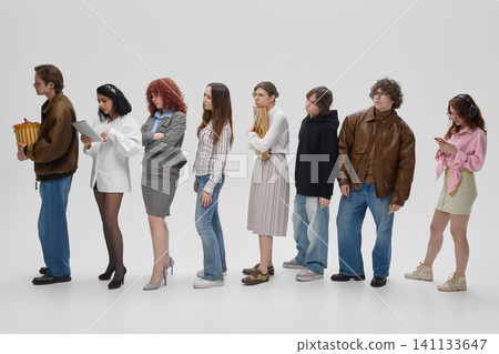 Diverse shoppers waiting in checkout line with bags and purchases in modern retail store. 141133647