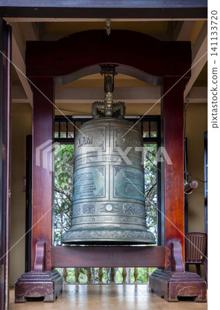 Large ornate bronze Buddhist bell hanging in a wooden frame at a Vietnamese temple featuring dragon decorations and engraved inscriptions in traditional Asian style. Large ornate bronze Buddhist bell hanging in a wooden frame at a Vietnamese temple featuring dragon decorations and engraved inscriptions in traditional Asian style. 141133720