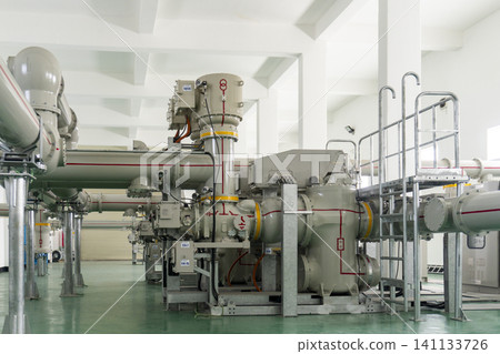 Gas-insulated switchgear GIS equipment inside an indoor electrical substation featuring gray high-voltage apparatus with yellow bands and red grounding markings aligned in a clean facility. 141133726