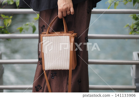 Woman holds a small bag while standing by water Woman holds a small bag while standing by water 141133906