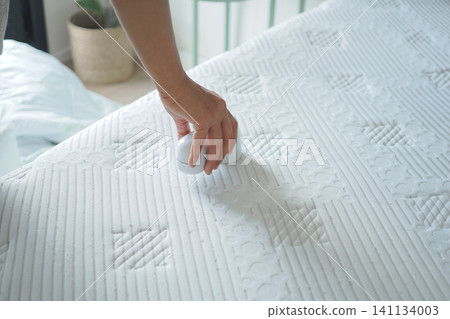 Person cleaning a mattress with a handheld device Person cleaning a mattress with a handheld device 141134003