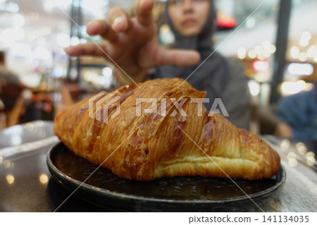 Person reaches for a croissant in a busy cafe setting Person reaches for a croissant in a busy cafe setting 141134035
