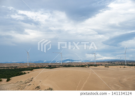 Wind turbines standing on vast sand dunes under an overcast cloudy sky Wind turbines standing on vast sand dunes under an overcast cloudy sky 141134124