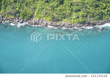 Top view of the tropical green forest and crystal clear turquoise ocean water crashing on the rocky shore in Phu Quoc, Vietnam. Top view of the tropical green forest and crystal clear turquoise ocean water crashing on the rocky shore in Phu Quoc, Vietnam. 141134126