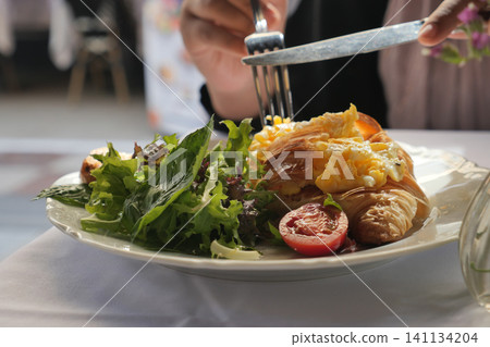 Enjoying a delicious meal with croissant and salad Enjoying a delicious meal with croissant and salad 141134204