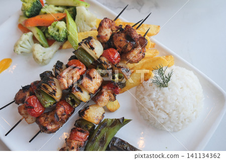 Grilled chicken skewers served with rice and vegetables 141134362
