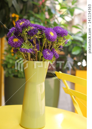 Bright purple flowers in a green vase on a sunny table 141134363