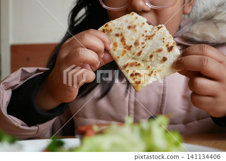 Child enjoying flatbread while seated at a table Child enjoying flatbread while seated at a table 141134406