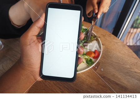 Holding a smartphone near fresh salad at a dining table Holding a smartphone near fresh salad at a dining table 141134413