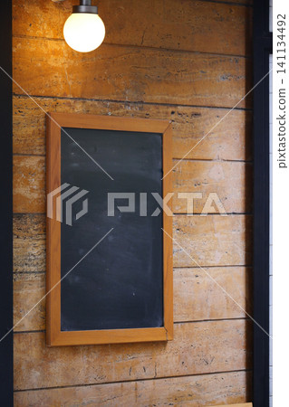 Empty chalkboard on wooden wall with warm light above Empty chalkboard on wooden wall with warm light above 141134492