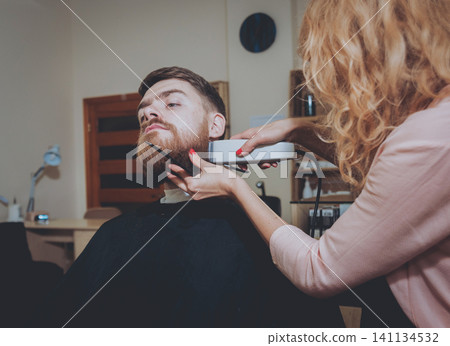 Master cuts hair and beard of men, hairdresser makes hairstyle for a young man. Hipsters 141134532