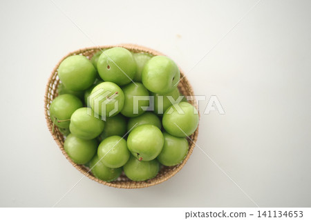 sour green plums in a woven basket on a light surface sour green plums in a woven basket on a light surface 141134653