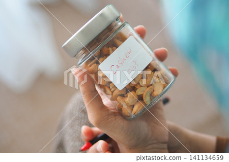 Person holding a jar of cashew nuts in a casual setting Person holding a jar of cashew nuts in a casual setting 141134659