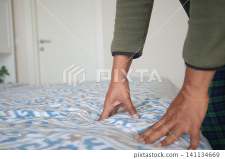 Making the bed with care in a simple room Making the bed with care in a simple room 141134669