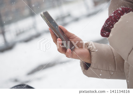 Person checks phone during snowfall in the city Person checks phone during snowfall in the city 141134816