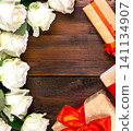 many white roses on a dark wooden background with a gift and a red bow, a mild day postcard, a Valentine's Day or a women's day. greeting card. place for text 141134907