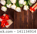 many white roses on a dark wooden background with a gift and a red bow, a mild day postcard, a Valentine's Day or a women's day. greeting card. place for text 141134914