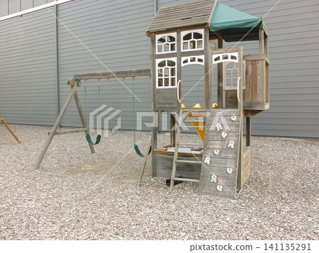 Wooden children playground set with swings and climbing wall on wood chip ground by a gray wall - June 6, 2026 Milton WA, USA Wooden children playground set with swings and climbing wall on wood chip ground by a gray wall - June 6, 2026 Milton WA, USA 141135291