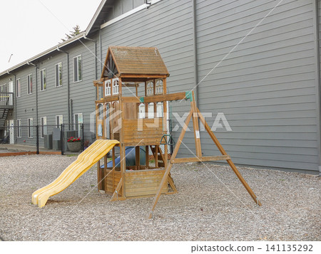 Wooden children playground set with swings and climbing wall on wood chip ground by a gray wall - June 6, 2026 Milton WA, USA Wooden children playground set with swings and climbing wall on wood chip ground by a gray wall - June 6, 2026 Milton WA, USA 141135292