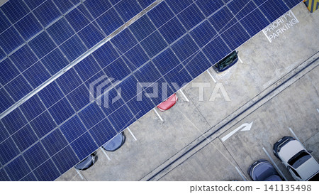 Solar roof. Aerial drone view of solar roof of carport or carpark. Photovoltaic panels covering a parking lot. Clean renewable energy infrastructure supports sustainable transportation. Solar energy Solar roof. Aerial drone view of solar roof of carport or carpark. Photovoltaic panels covering a parking lot. Clean renewable energy infrastructure supports sustainable transportation. Solar energy 141135498