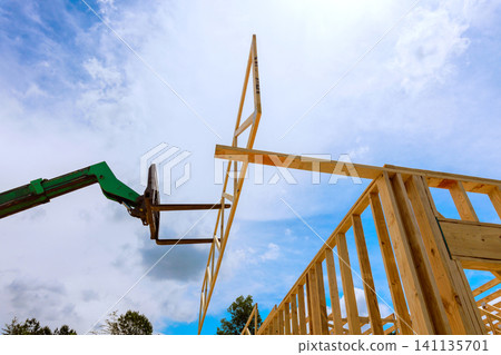 Construction workers use machine to lift wooden frame into place at building 141135701