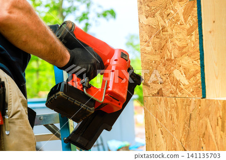 Worker uses nail gun to fasten wood panels at construction site Worker uses nail gun to fasten wood panels at construction site 141135703