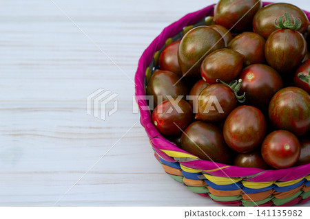 Dark cherry tomatoes in the palm basket on the white table. Dark cherry tomatoes in the palm basket on the white table. 141135982