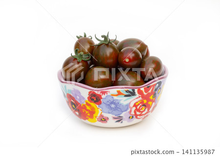 Ceramic floral bowl with dark cherry tomatoes on white. Ceramic floral bowl with dark cherry tomatoes on white. 141135987