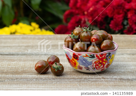 Bowl with black cherry tomatoes in the summer blooming garden. Bowl with black cherry tomatoes in the summer blooming garden. 141135989