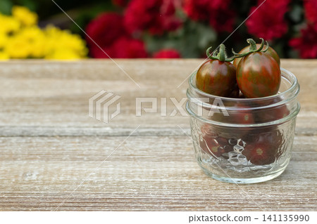 Jar with black cherry tomatoes in the summer blooming garden. Jar with black cherry tomatoes in the summer blooming garden. 141135990