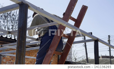 Adult worker polishing iron using electric grinder wheel on carport frame. Professional repairman grinding metal detail with circular saw at construction at sunny day. Male laborer working at the site Adult worker polishing iron using electric grinder wheel on carport frame. Professional repairman grinding metal detail with circular saw at construction at sunny day. Male laborer working at the site 141136265