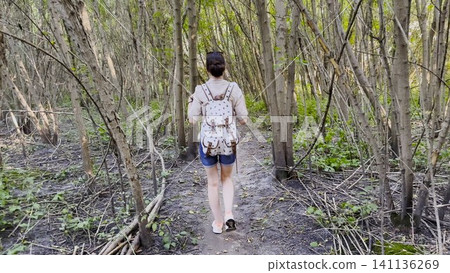 Young girl going along path at mangrove forest. Female hiker with backpack walking among trail at wild nature. The scene reflecting adventure, travel and connection with wild nature. Slow motion Young girl going along path at mangrove forest. Female hiker with backpack walking among trail at wild nature. The scene reflecting adventure, travel and connection with wild nature. Slow motion 141136269