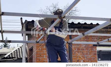Adult worker polishing iron using electric grinder wheel on carport frame. Professional repairman grinding metal detail with circular saw at construction at sunny day. Male laborer working at the site Adult worker polishing iron using electric grinder wheel on carport frame. Professional repairman grinding metal detail with circular saw at construction at sunny day. Male laborer working at the site 141136272