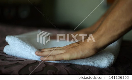 Male hands of housekeeping adjusting soft white terry towel on a neatly made bed in a modern hotel room. Service personnel preparing clean bedding and hospitality interior for guest accommodation Male hands of housekeeping adjusting soft white terry towel on a neatly made bed in a modern hotel room. Service personnel preparing clean bedding and hospitality interior for guest accommodation 141136303