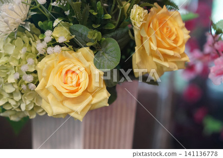 closeup beautiful large yellow roses flower and white and green flowers bouquet in white ceramic vase, blur background, nature, fashion, love, decor, valentine closeup beautiful large yellow roses flower and white and green flowers bouquet in white ceramic vase, blur background, nature, fashion, love, decor, valentine 141136778