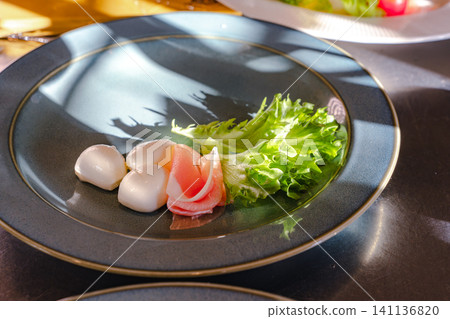 A healthy appetizer of mozzarella, prosciutto, and lettuce served on a blue plate. A healthy appetizer of mozzarella, prosciutto, and lettuce served on a blue plate. 141136820