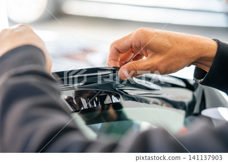 A car wrapping specialist applies a polyurethane film to the car. Detailer PPF 141137903