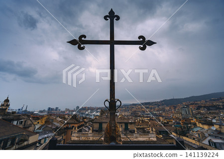 Genoa, Italy - Nov 4 2018, panoramic view of the city from roof of Cathedral of Saint Lawrence, with a giant metal Catholic cross in foreground, during the daytime with a cloudy sky, Genoa, Italy Genoa, Italy - Nov 4 2018, panoramic view of the city from roof of Cathedral of Saint Lawrence, with a giant metal Catholic cross in foreground, during the daytime with a cloudy sky, Genoa, Italy 141139224