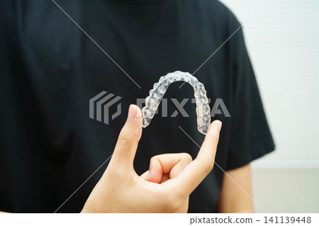 Man holding invisible aligner orthodontic retainer for dental teeth straightening. Man holding invisible aligner orthodontic retainer for dental teeth straightening. 141139448