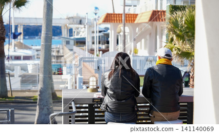 The backs of a couple sitting in a cafe overlooking the marina. The backs of a couple sitting in a cafe overlooking the marina. 141140069