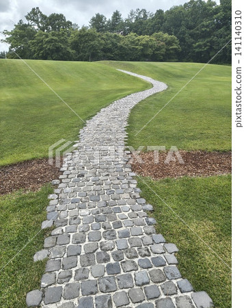 A cobblestone path winds through the green hills in an S-shape, under a cloudy sky. A cobblestone path winds through the green hills in an S-shape, under a cloudy sky. 141140310