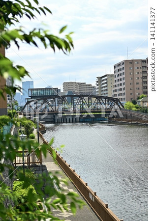 沿著運河的步道和橫跨河流的桁架橋,周圍環繞著城市公寓大樓和辦公大樓。 沿著運河的步道和橫跨河流的桁架橋,周圍環繞著城市公寓大樓和辦公大樓。 141141377